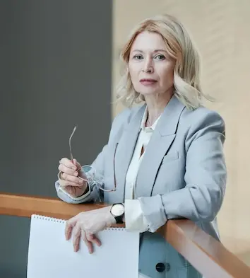 The Dean of Beckminster Crest, a professional woman wearing a suit and holding notes.